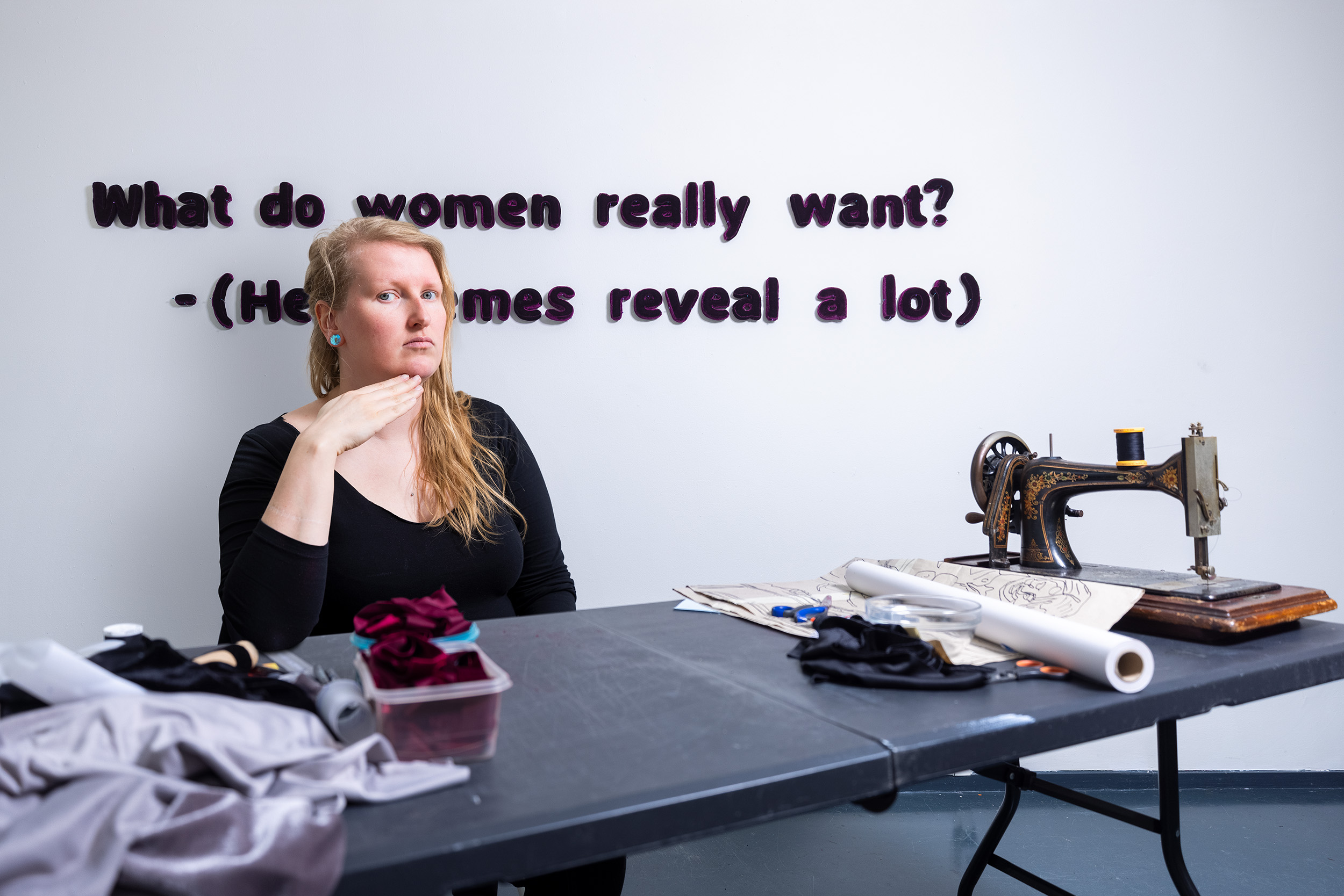 Joyce Overheul poseert zittend aan haar naaitafel met achter haar op de muur de tekst: What do women really want? (Her memes reveal a lot)